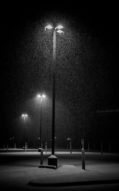 a black and white photo of a street light in the dark with snow falling on it