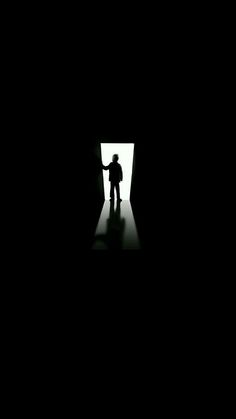 a person standing in a dark room with their hand out to the light at the end