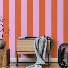 an orange and pink striped wall next to a wooden table with a gray blanket on it