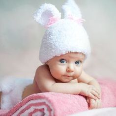 a baby laying on top of a pink blanket wearing a white bunny ears hat and smiling at the camera