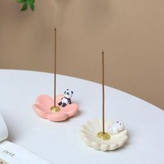 there are two small toothbrush holders on top of a white table next to a plant