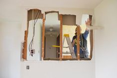 a woman standing in the middle of a room that has been torn down and is holding a hammer