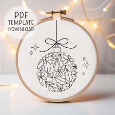 a cross stitch christmas ornament hanging from a hoop with lights in the background