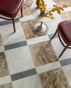 two chairs and a table on a checkered tile floor with a vase in the middle