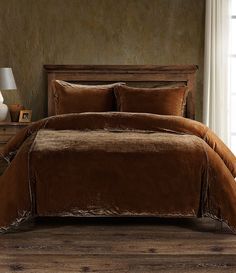 a bed with brown comforter and pillows in a room next to a lamp on a table