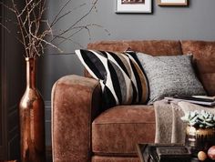 a living room with a brown couch and two vases filled with flowers on the table