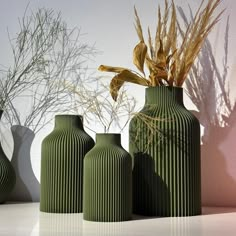 three green vases sitting next to each other on a white table with plants in them