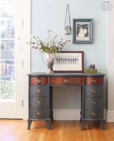 a desk with drawers and flowers on it in front of a framed photo, near a door