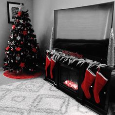 a black and white photo of a christmas tree with stockings on the fire place next to it