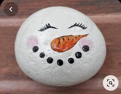 a painted rock with eyes, nose and orange carrot on it's face sitting on a wooden surface