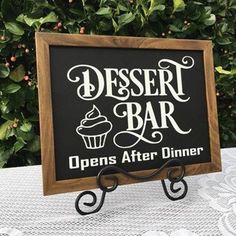 a dessert bar sign sitting on top of a table next to some bushes and trees