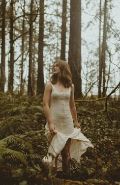 a woman in a white dress is walking through the woods with her hands on her hips