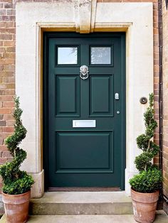 a green front door with two potted plants