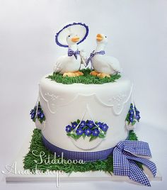 two white ducks sitting on top of a cake with green grass and blue ribbon around it