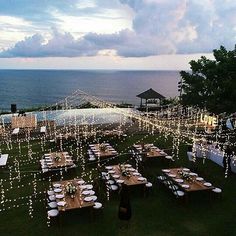 an outdoor dining area overlooking the ocean with lights strung from it and tables set up for dinner