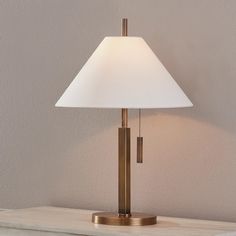 a lamp that is sitting on top of a table next to a white vase and a wall