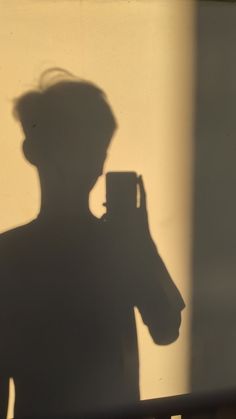 the shadow of a man holding a camera in front of a mirror with his head turned to the side