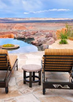 two lawn chairs sitting on top of a stone patio next to a swimming pool in the desert