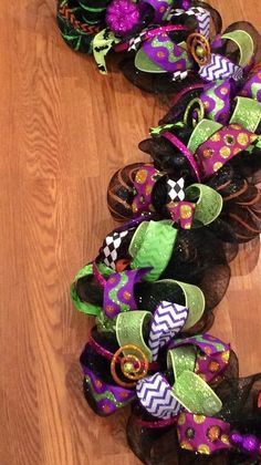 a close up of a wreath on a wooden floor with purple, green and black decorations