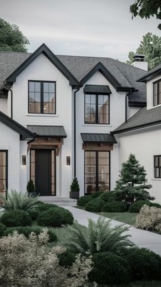 a large white house with black trim and lots of windows on the front door is surrounded by greenery