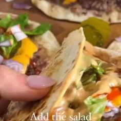 a hand holding a tortilla filled with meat and veggies on top of it