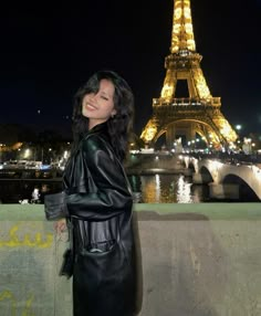 a woman standing in front of the eiffel tower at night with her hands on her hips