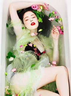 a woman laying in a tub with flowers on her head