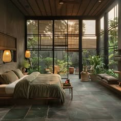 a bedroom with stone flooring and large windows overlooking the garden area is lit by lamps