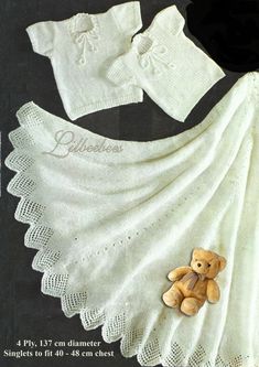 a teddy bear sitting on top of a white blanket next to a knitted outfit