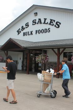 two men pushing a shopping cart in front of a building with an e & s sales sign on it