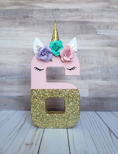 a pink and gold unicorn shaped box with flowers on it's head, sitting on top of a wooden table