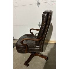 a brown leather office chair sitting on top of a hard wood floor next to a white wall