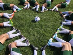 a group of young people laying on top of a lush green field next to a soccer ball