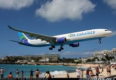 an airplane taking off from the beach with people standing on the sand and in the water