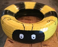 a yellow and black tire sitting on top of a piece of wood with eyes painted on it