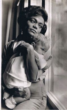 an old black and white photo of a woman holding a baby in her arms while looking out the window