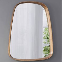 a wooden mirror hanging on the wall next to a potted plant in front of a window