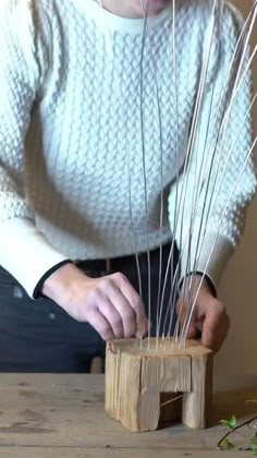 a woman is making reeds out of wood on a wooden table in front of her