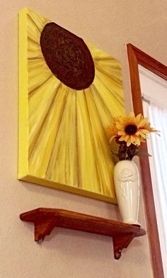 a sunflower in a vase sitting on a shelf next to a framed art piece