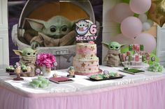 a baby yoda cake and other decorations on a table with balloons in the background