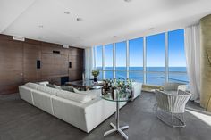 a living room filled with white furniture and large windows overlooking the ocean on a sunny day