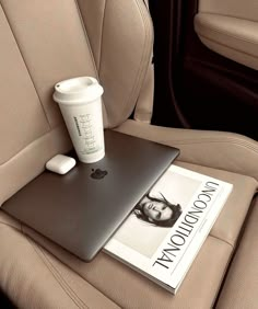 a laptop computer sitting on top of a car seat next to a cup of coffee