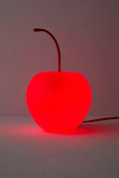 a red apple shaped lamp sitting on top of a white table next to a gray wall