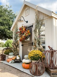 pumpkins and gourds are arranged on the front porch of a small white house