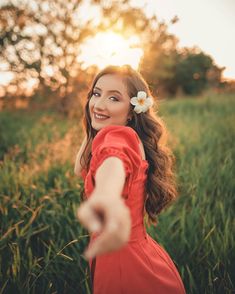 a woman in a red dress is smiling and pointing her finger at the camera with a flower in her hair