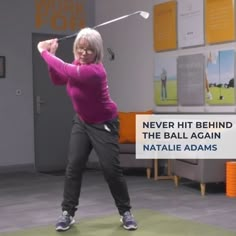 an older woman swinging a golf club in a room with posters on the wall behind her