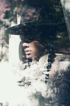 a woman wearing a black hat and dress in the back seat of a car with trees behind her