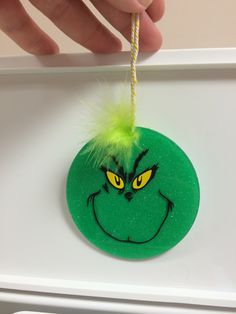 a hand holding a green ornament with an angry grin face and yellow eyes