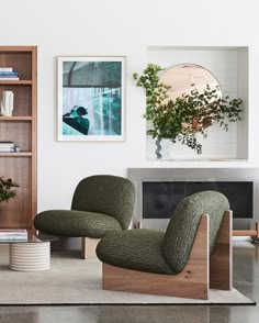 a living room with two green chairs and a book shelf on the wall next to a fireplace