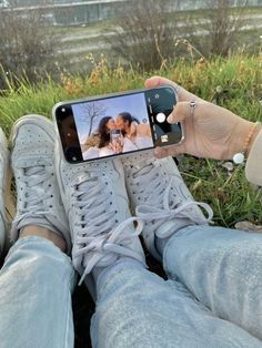 someone taking a selfie with their cell phone while sitting in the grass near some water